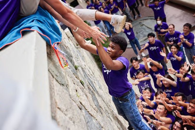 Students cheering a classmate scaling a wall